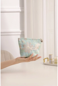 Macro detail of a light blue floral jacquard makeup bag with a gold flower zipper pull