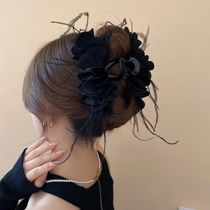 Detailed view of a black layered floral hair claw clip with feathers on braided hair