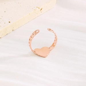 Détail de la bague cœur or rose avec anneau en chaîne sur tissu texturé blanc