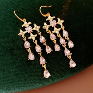 Macro detail of gold tassel earrings with pink heart crystals on dark velvet fabric