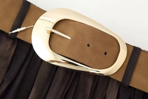 Dettaglio di cintura in pelle scamosciata marrone con fibbia dorata su gonna a pieghe