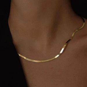 Detailed view of a sleek golden snake bone chain necklace on a model collarbone