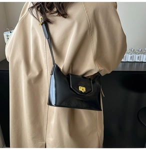 Detail of black glossy faux leather shoulder bag featuring a gold metal buckle closure