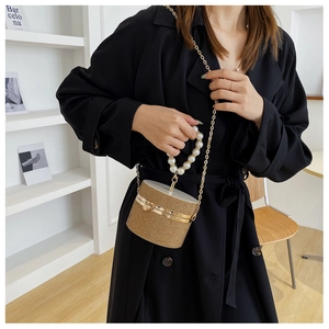 Close-up of golden woven cylinder handbag with pearl handle and metal chain detail