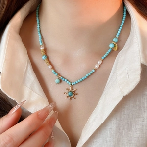 Détail du collier avec pendentif soleil, perles turquoise et petit médaillon doré