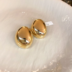 Macro shot of gold-plated pebble earrings with a polished mirror finish on white ceramic