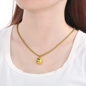 Close-up of a hollow golden sphere pendant on a square snake chain worn by a model