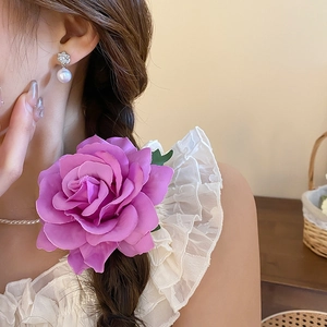 Close-up of a large purple fabric rose hair clip and matching pearl drop earrings on a model