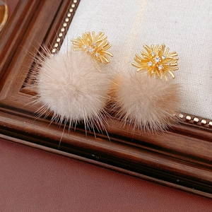 Detailed view of gold floral stud earrings with rhinestones and soft beige fur pompoms