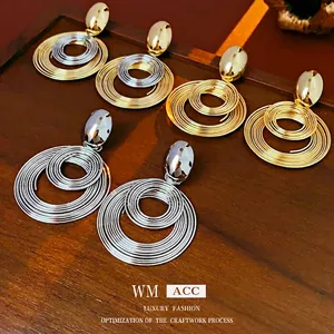 Exaggerated golden and silver coiled metal hoop earrings with oval studs on wood