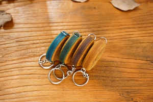 Close-up of four vintage embossed leather tape measures in various colors on wood