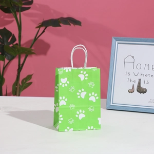 Green party gift bag with white paw prints and handles on a pink lifestyle background