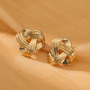 Macro detail of gold-tone knot stud earrings on orange satin showing metallic texture