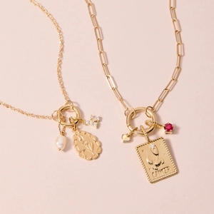 Gold cancer zodiac pendant necklace with red gemstone and pearls on a pink background