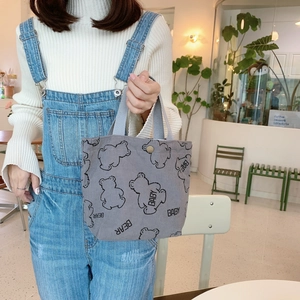 Gray corduroy tote lunch bag with cute bear print and lettering in a cozy cafe setting