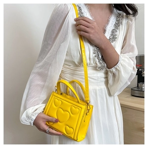 Détail du sac à bandoulière jaune avec motif cœur embossé et finitions dorées sur modèle