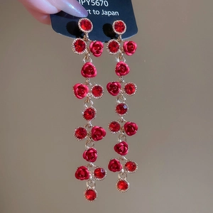 Detail of red rose drop earrings with tassel and gold metal links on a black card