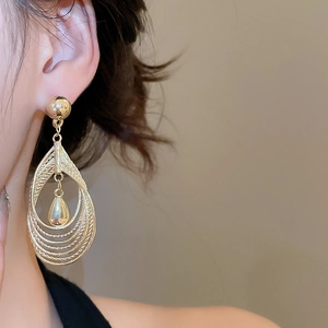 Detail of layered gold teardrop earrings featuring hollow textured frames and polished drop