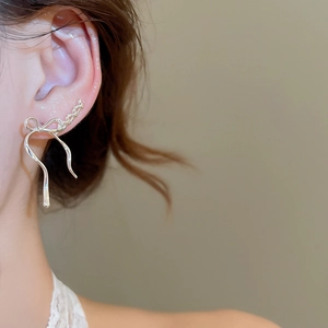 Close-up of elegant silver bow ribbon ear climber earrings with long flowing metallic strands
