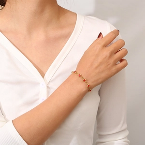 Detail of gold chain bracelet with red round zircon and star charms on woman's wrist