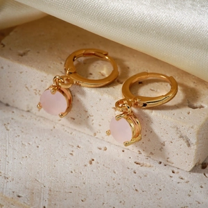 Elegant gold hoop earrings with pink round crystal pendants on a textured stone base