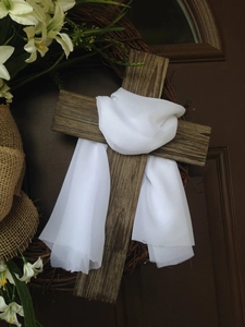 Detail of wooden cross with white fabric drape and lilies on a rustic Easter wreath