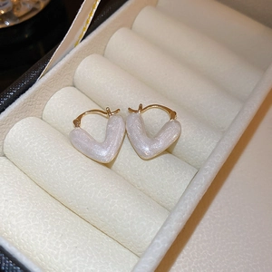 Detail of heart-shaped gold earrings with white pearlescent inlay in a white jewelry box