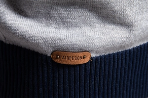 Detailaufnahme der grauen und blauen Strickstruktur mit genietetem Lederaufnäher am Saum