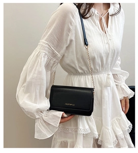Detail of minimalist black leather crossbody bag with gold chain strap on white lace dress