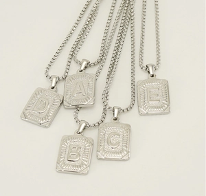 Macro view of silver rectangular letter pendants with radial textures on pearl chains