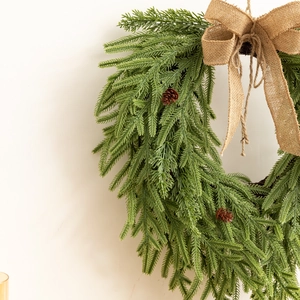 Couronne de Noël artificielle avec pommes de pin et grand nœud en jute sur un mur blanc