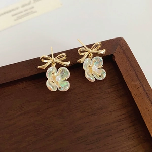 Detail of gold bow earrings featuring iridescent petals and a central pearl accent
