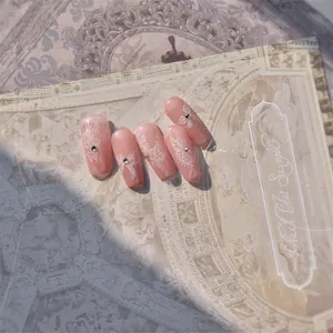 Detailed close-up of pink gradient press-on nails with butterfly floral art and rhinestones