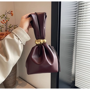Close-up of wine red pleated cloud bag with elegant gold ring handle in hand