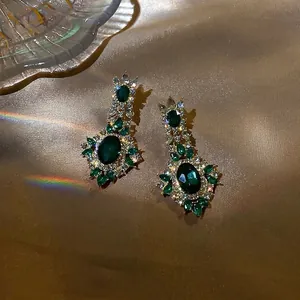 Vintage emerald-style silver needle earrings with shimmering crystals on gold silk background