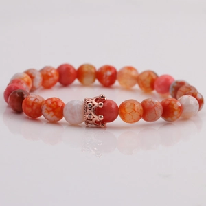 Macro detail of 8mm faceted orange stones with a rose gold crown charm on a mirror surface