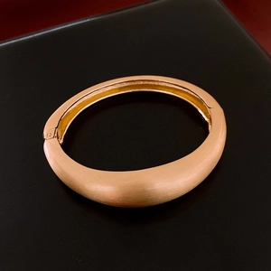 Détail du bracelet rigide en métal or rose mat avec surface large et fermoir à charnière précise