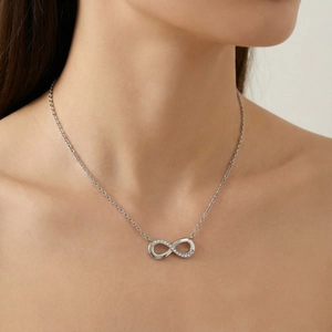 Close-up of a silver infinity pendant necklace with small crystals on a model's neck