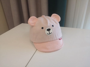 Detail of pink and white striped baby baseball cap with 3D bear ears on a white surface