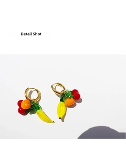 Detail shot of fruit-shaped charms on 18K gold plated hoop earrings with glossy finish