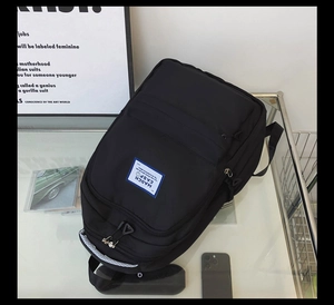 Macro view of a large black nylon backpack featuring a blue brand woven label on glass