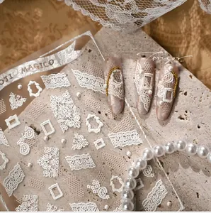 Macro shot of 3D embossed white lace nail stickers with pearl and vintage frame details