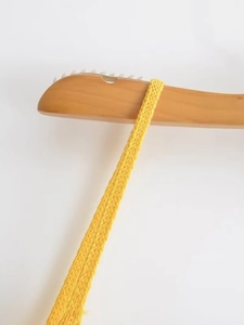 Detaillierte Nahaufnahme des gelben Strickriemens auf einem hochwertigen Holzkleiderbügel