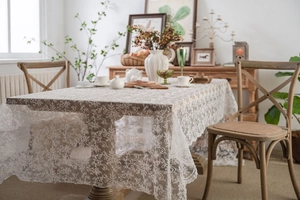 Detailed close-up of white lace tablecloth with intricate floral embroidery on wood table