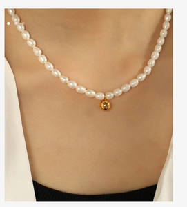 Close-up of Baroque pearl necklace featuring a gold ball pendant on a female collarbone