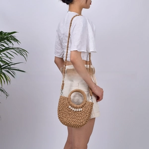 Detail of handmade straw crossbody bag with shell trim and woven handles on a model