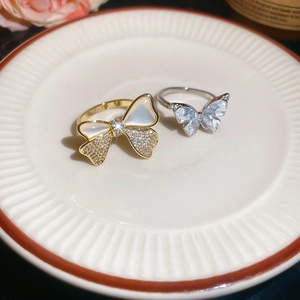 Macro view of 14k gold plated bow and flower rings with shell and zircon details