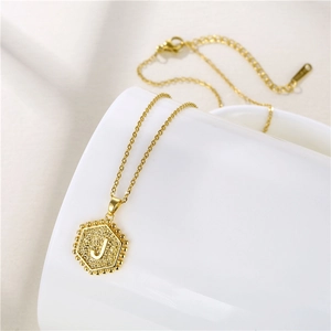 Macro shot of gold hexagon necklace with letter J pendant on white ceramic base