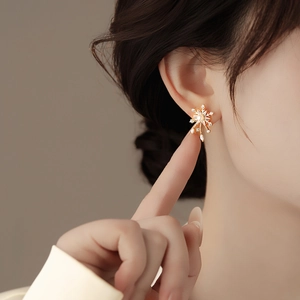 Close-up of gold snowflake stud earrings with a central pearl and sparkling zircon stones