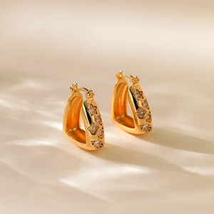 Detail of gold-plated star and zircon earrings on a soft beige fabric background